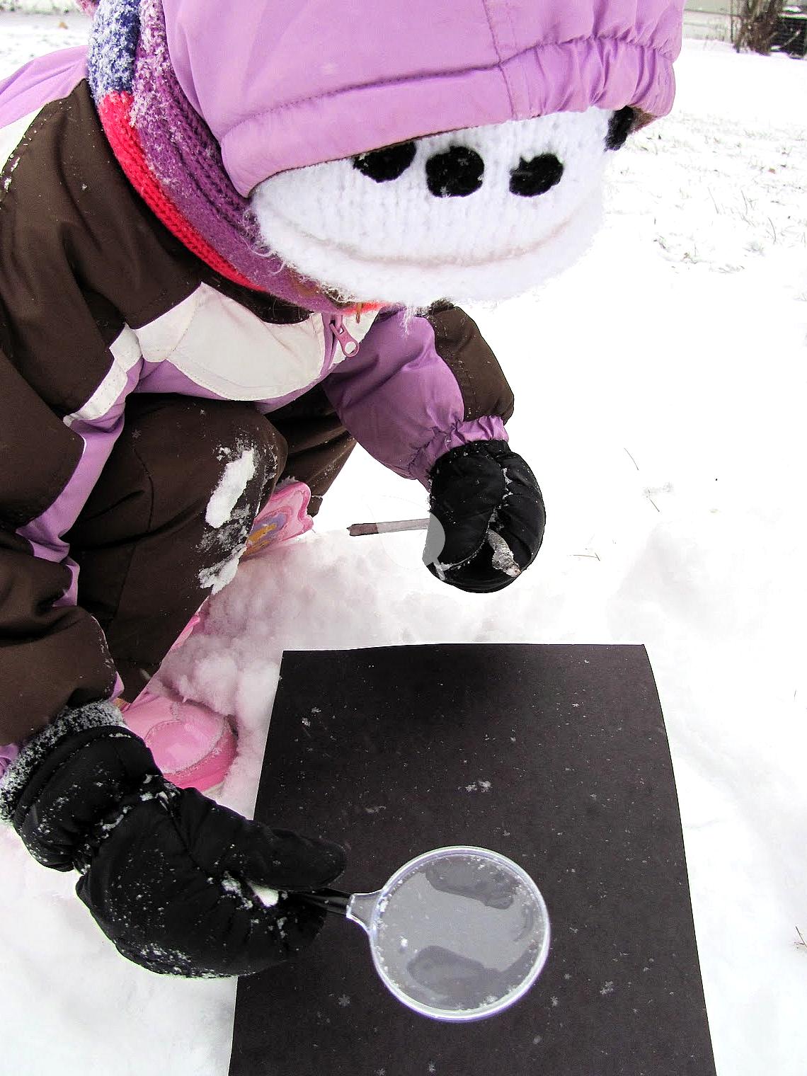 Child observing a snowflake with magnifier